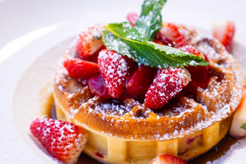 Belgian-style stuffed waffle topped with sliced strawberries, powdered sugar and mint on a white plate at Djon Djon, Brooklyn