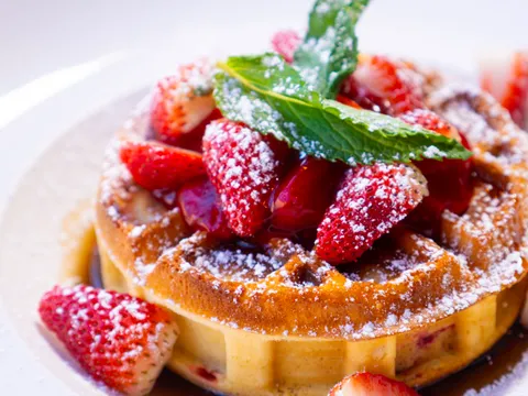 Belgian-style stuffed waffle topped with sliced strawberries, powdered sugar and mint on a white plate at Djon Djon, Brooklyn