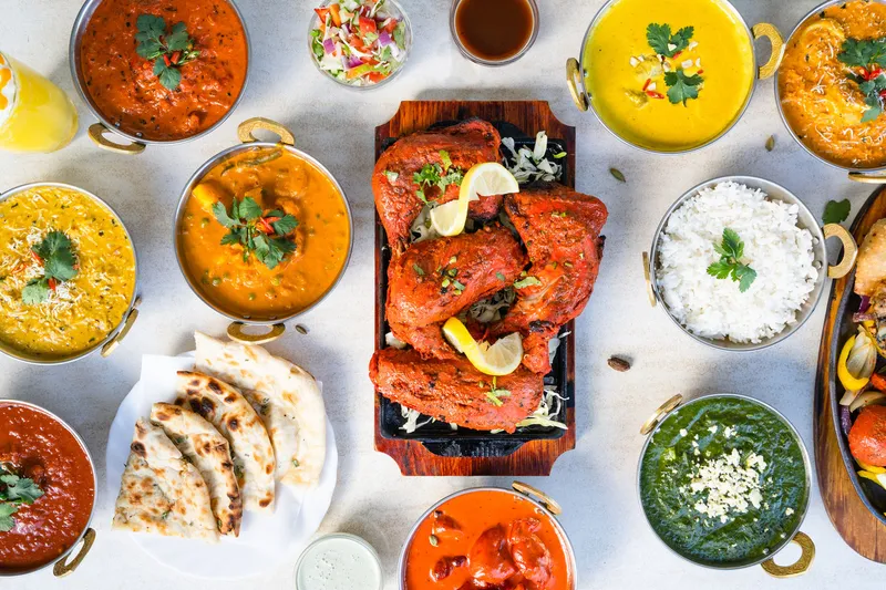 An overhead spread of Indian dishes at Nizami Biryani & Grill in Agoura Hills, California — a sizzler of tandoori chicken surrounded by curries in copper karahis, basmati rice, naan and saag