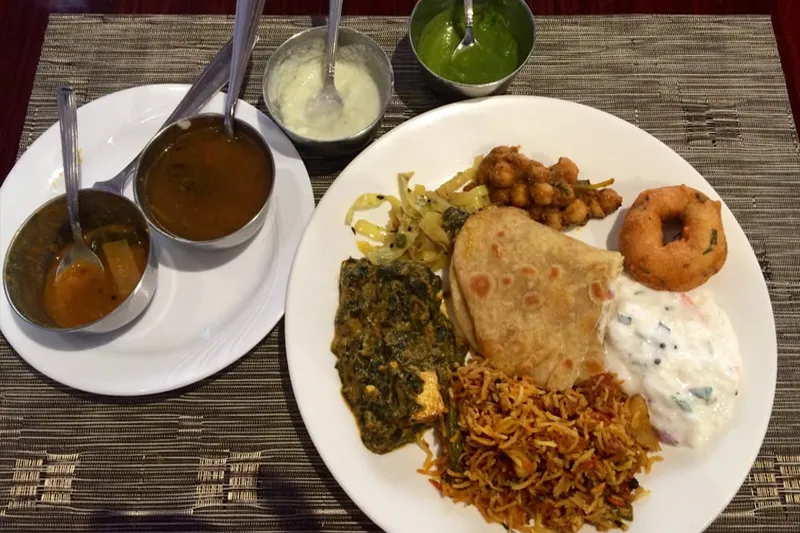 South Indian sampler plate at Dosa World in Hicksville with bowls of sambar, rasam and chutney alongside biryani, saag, chana, vada, raita and roti