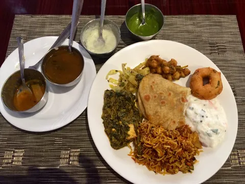 South Indian sampler plate at Dosa World in Hicksville with bowls of sambar, rasam and chutney alongside biryani, saag, chana, vada, raita and roti
