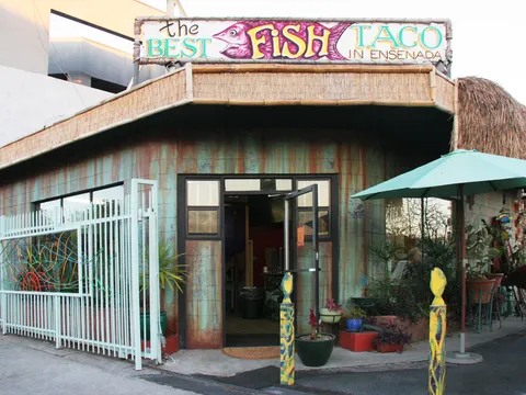 Palapa-roofed corner storefront of Best Fish Taco In Ensenada in Los Feliz, Los Angeles, with its hand-painted fish sign and patio umbrella