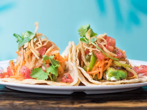 Two street-style tacos topped with pico de gallo, shredded carrot and crispy potato on a white plate at Broken English Taco Pub