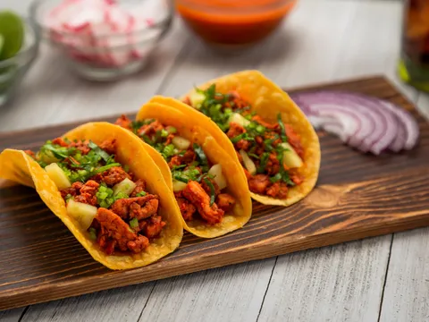 Three al pastor tacos on corn tortillas topped with pineapple, cilantro and onion on a wooden board at Tacos Don Cuco in El Paso