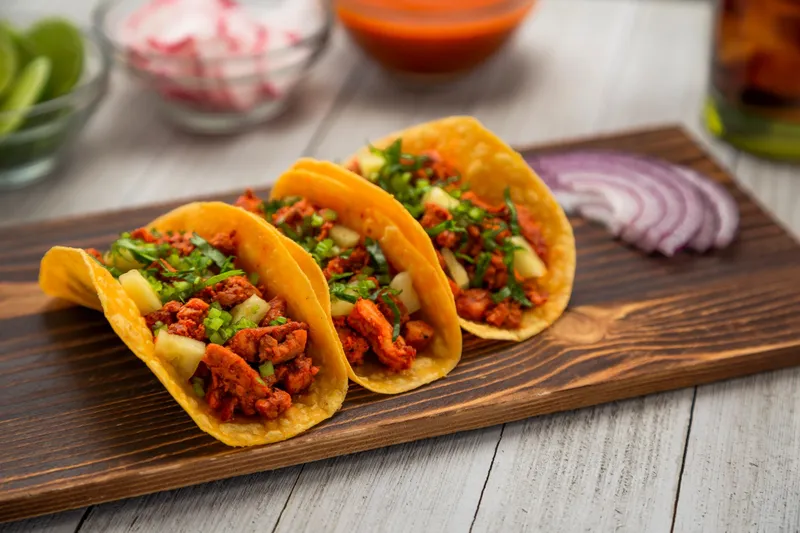 Three al pastor tacos on corn tortillas topped with pineapple, cilantro and onion on a wooden board at Tacos Don Cuco in El Paso