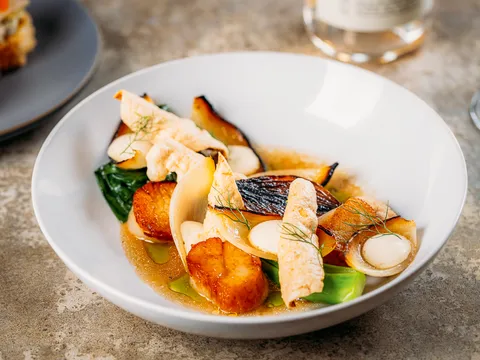 Seared scallops with mushrooms, greens, and broth in a white bowl at The Antler Room in Kansas City.