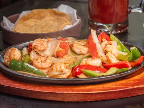 Shrimp fajitas with red and green bell peppers and onions on a cast-iron skillet at Señor López, served with a basket of warm tortillas
