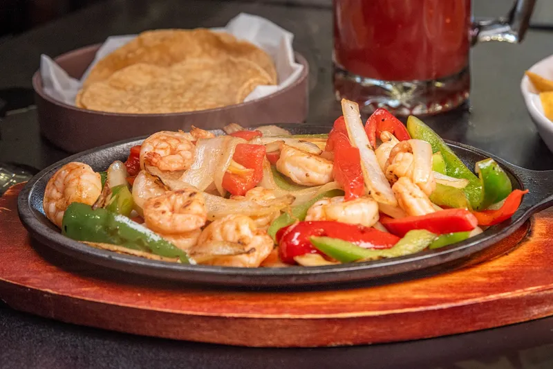Shrimp fajitas with red and green bell peppers and onions on a cast-iron skillet at Señor López, served with a basket of warm tortillas