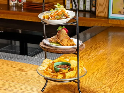 A three-tier stand holding chips and salsa, a filled empanada, and a plated appetizer at Bar Mexicana in New York