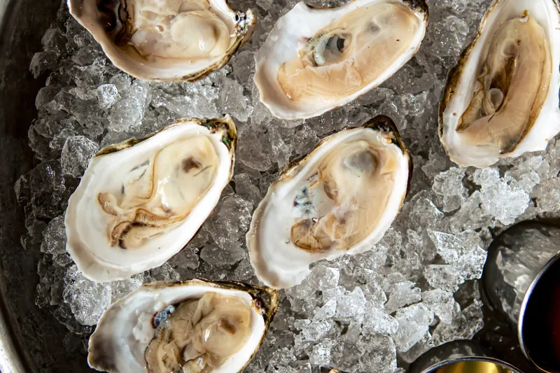 A metal tray of freshly shucked oysters on crushed ice with mignonette spoons at Hen of the Wood in Burlington
