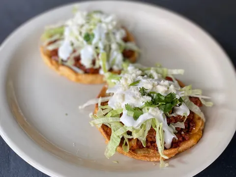 Two sopes topped with chorizo, shredded lettuce, crema, cilantro, and queso fresco on a white plate at Fonda La Catrina in Seattle