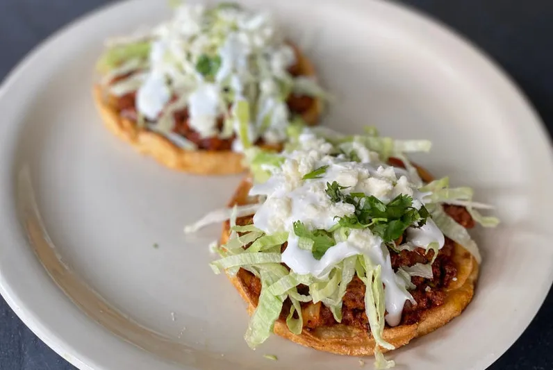 Two sopes topped with chorizo, shredded lettuce, crema, cilantro, and queso fresco on a white plate at Fonda La Catrina in Seattle