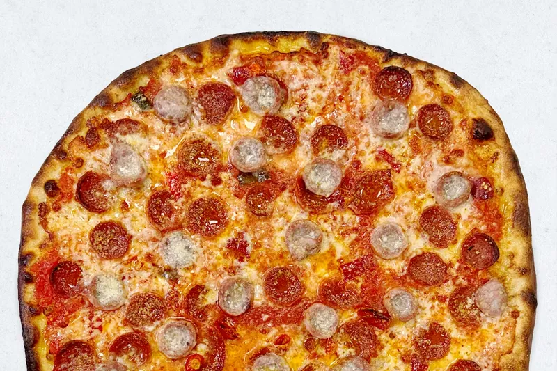 A coal-fired Frank Pepe pizza topped with pepperoni and sausage on a thin charred crust
