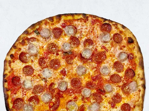 A coal-fired Frank Pepe pizza topped with pepperoni and sausage on a thin charred crust