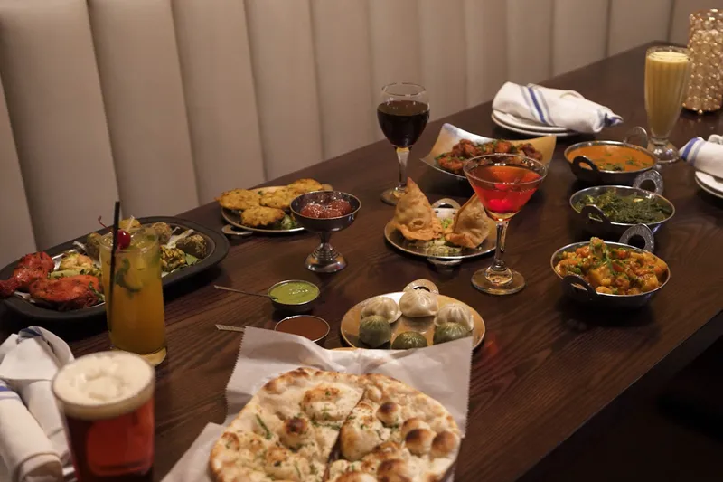 Table spread of curries, momos, tandoori chicken, naan and drinks in a booth at Saffron Indian Grill