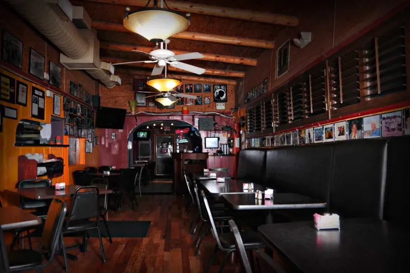 Empty wood-floored dining room at L&J Cafe in El Paso, with black vinyl booths and walls covered in framed photographs