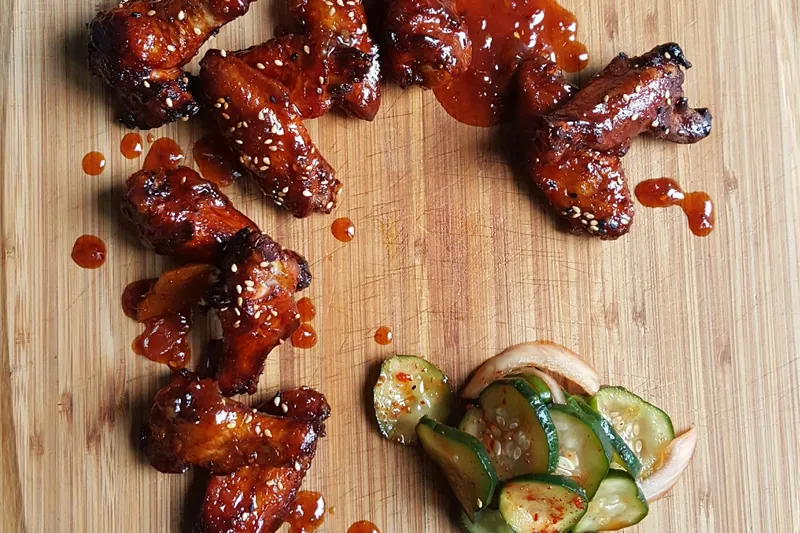 Gochujang-glazed smoked chicken wings with sesame seeds and cucumber kimchi on a wood board at Heirloom Market BBQ in Atlanta