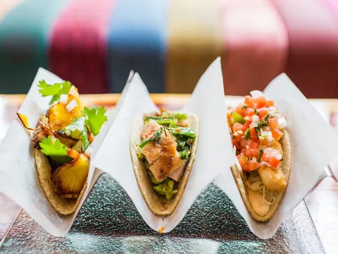 Three tacos in paper holders on a wooden table at Oyamel in Washington, DC