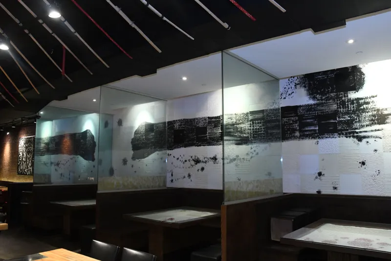 Interior dining room at IPPUDO NY East Village with wood booths, glass partitions and black-and-white brushstroke wall panels