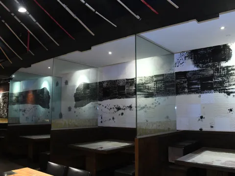 Interior dining room at IPPUDO NY East Village with wood booths, glass partitions and black-and-white brushstroke wall panels
