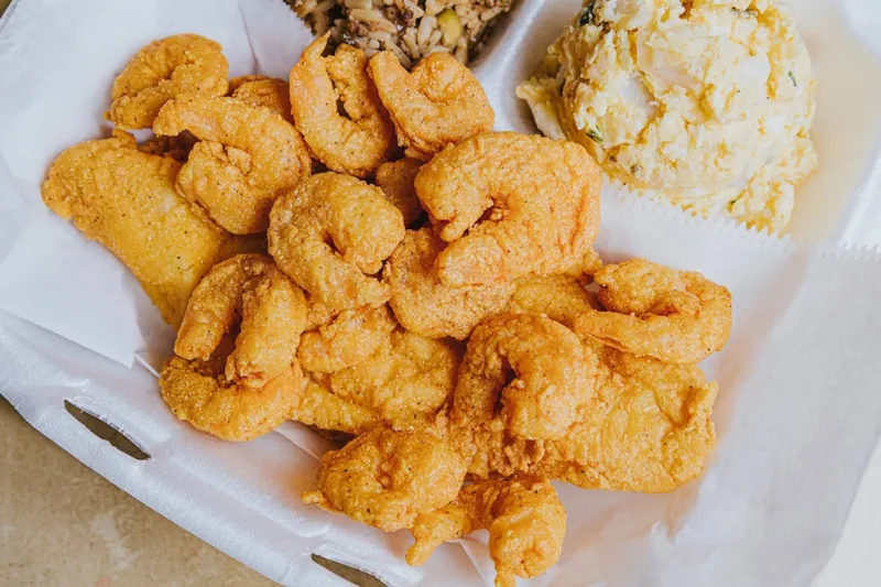 Fried shrimp and catfish platter with dirty rice and potato salad in a takeout container at Li'l Dizzy's Cafe