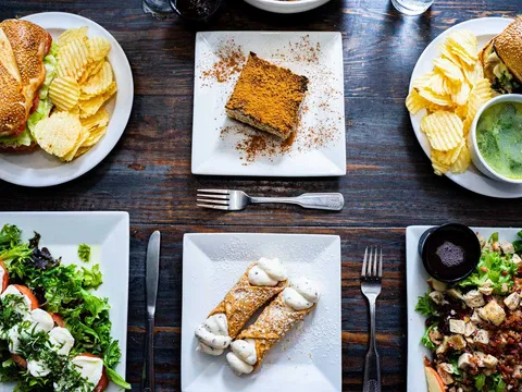 Sandwiches, salads and desserts arranged on a dark wooden table at Rocco Italian Grill