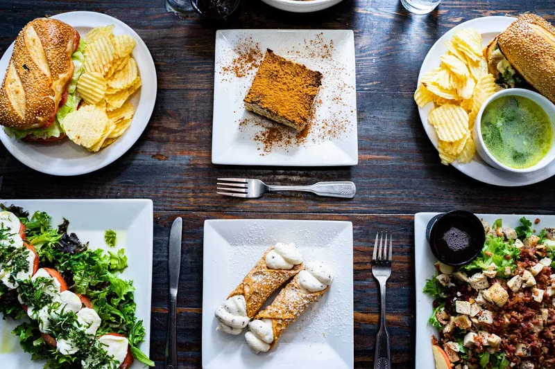 Sandwiches, salads and desserts arranged on a dark wooden table at Rocco Italian Grill