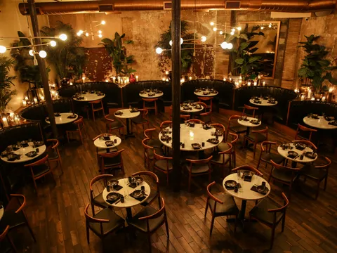 Candlelit dining room at Chinese Tuxedo with marble-topped tables, green leather banquettes, hanging bulb chandeliers and exposed brick walls