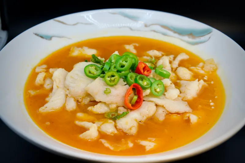 Sliced fish fillet in golden sauce topped with sliced green and red chilies and scallions in a white bowl at China Mama in Las Vegas