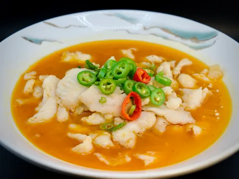 Sliced fish fillet in golden sauce topped with sliced green and red chilies and scallions in a white bowl at China Mama in Las Vegas