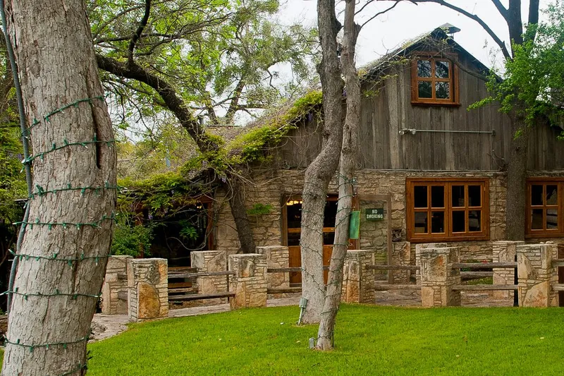 The stone-and-timber restaurant building of The Salt Lick BBQ set among oak trees in Driftwood, Texas