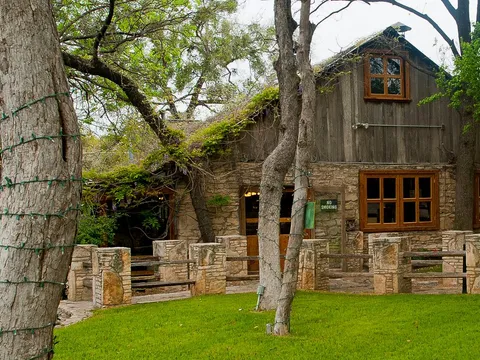The stone-and-timber restaurant building of The Salt Lick BBQ set among oak trees in Driftwood, Texas