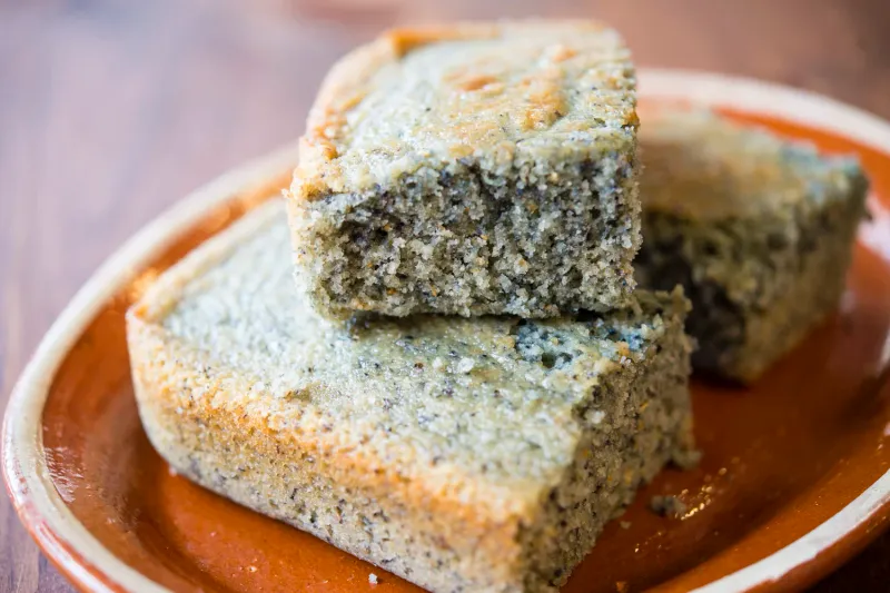 Two thick slices of Alta Baja Market's New Mexican blue corn cornbread stacked on a rustic terracotta plate