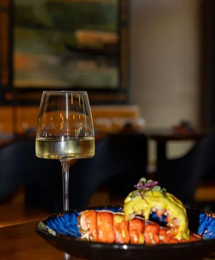 Plated lobster dish with a saffron-yellow sauce in a blue bowl, served beside a glass of white wine at Rivayat Creative Indian in Charleston