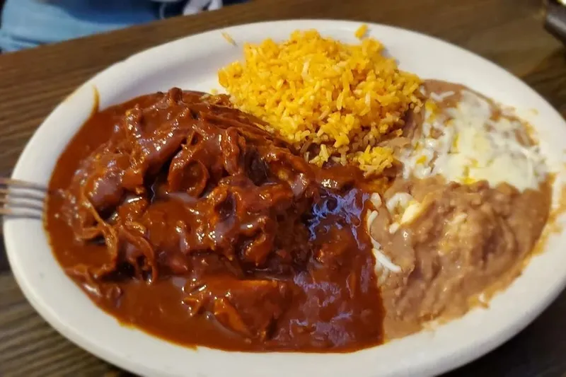 Plate of chicken mole with Spanish rice and refried beans topped with melted cheese at Kiki's Mexican Restaurant in El Paso
