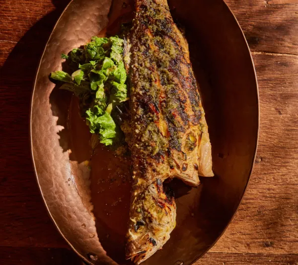 Kokkari Estiatorio's whole grilled fish on a hammered copper platter with a side of greens