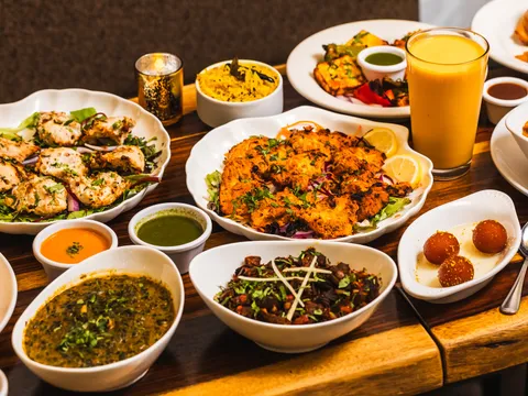 Tandoori platter, curries and mango lassi spread across a wooden table at Bombay's