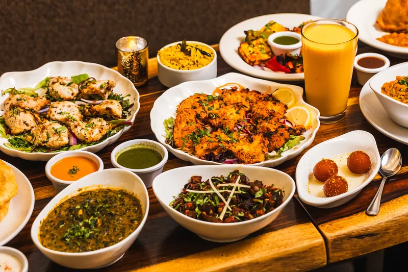 Tandoori platter, curries and mango lassi spread across a wooden table at Bombay's