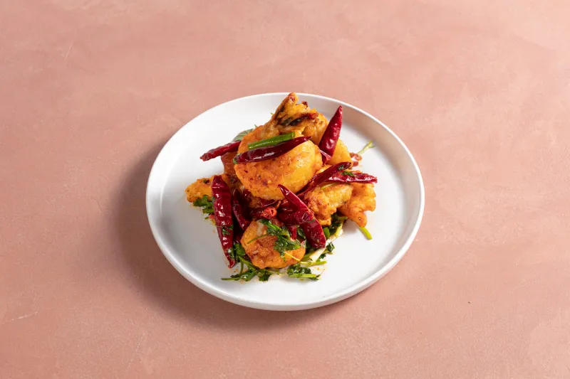 Sichuan-style crispy battered fish tossed with dried red chilies and cilantro on a white plate at Chang Chang