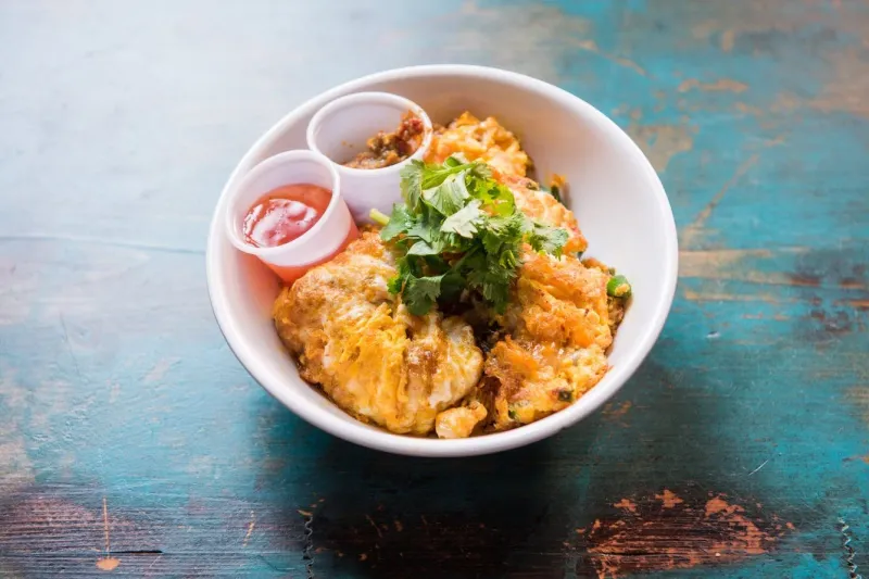 Oh Chien pan-fried oyster omelette topped with cilantro, served with chili sauces at Kopitiam