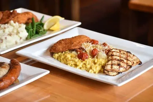 Two white platters of food at Penn Brewery in Pittsburgh: breaded schnitzel with grilled chicken, saffron spaetzle, roasted tomatoes and parmesan on one plate, and schnitzel with mashed potatoes and green beans behind