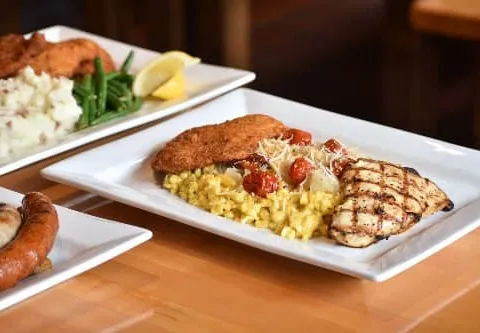 Two white platters of food at Penn Brewery in Pittsburgh: breaded schnitzel with grilled chicken, saffron spaetzle, roasted tomatoes and parmesan on one plate, and schnitzel with mashed potatoes and green beans behind