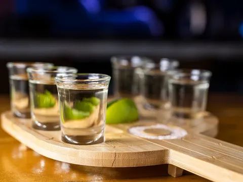 Row of tequila shots with lime on a wooden board at Kompali Taqueria