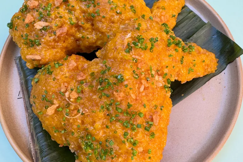 Golden fried chicken pieces served on a banana leaf and stoneware plate at Lasita