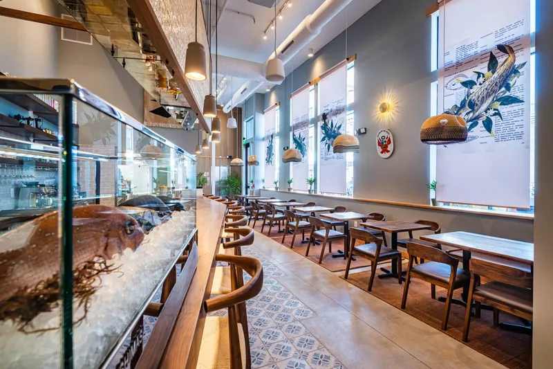 Dining room at Causa in Washington, DC with a fresh-fish display case on ice, a wooden counter with chairs, patterned tile floor, and Peruvian fish illustrations in the windows