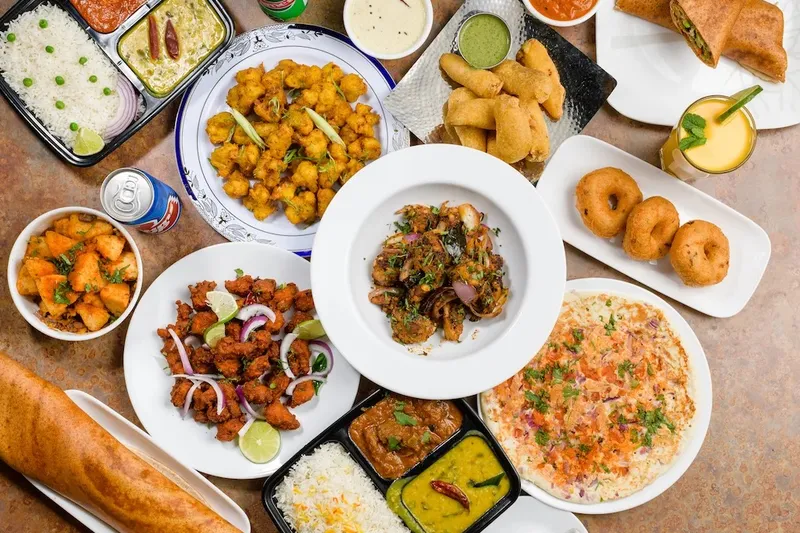 Overhead spread of South Indian dishes at NALA'S: a paper-thin dosa, idli and vada, thali trays with rice and curries, chicken 65, samosas, medu vada, mango lassi and a cup of masala chai