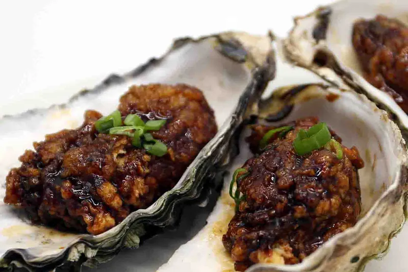 Two deep-fried oysters glazed in sauce and served in their shells, topped with scallions, at New Winsor Dim Sum House & Bar in Quincy