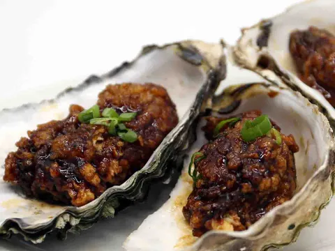 Two deep-fried oysters glazed in sauce and served in their shells, topped with scallions, at New Winsor Dim Sum House & Bar in Quincy