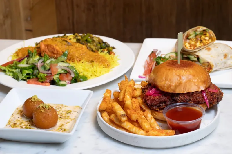 Spread of Bindaas Bowls & Rolls dishes: a chicken farcha burger with gunpowder fries, paneer rolls, a salmon bowl over lemon rice with kachumber salad, and gulab jamun with rabdi