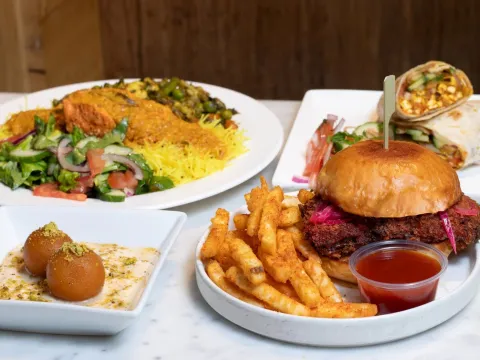 Spread of Bindaas Bowls & Rolls dishes: a chicken farcha burger with gunpowder fries, paneer rolls, a salmon bowl over lemon rice with kachumber salad, and gulab jamun with rabdi